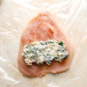 a portion of chicken roulade filling on a raw seasoned chicken breast.