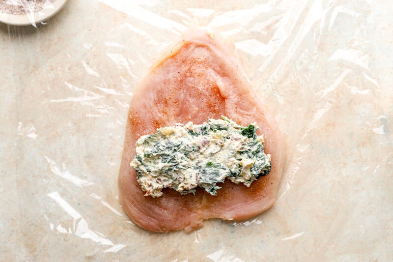 a portion of chicken roulade filling on a raw seasoned chicken breast.