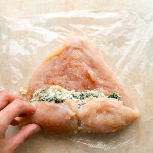 rolling a raw seasoned chicken breast to contain filling.