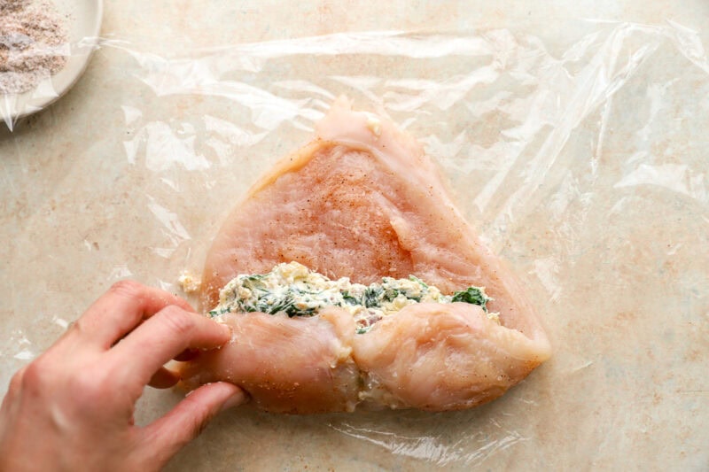 rolling a raw seasoned chicken breast to contain filling.