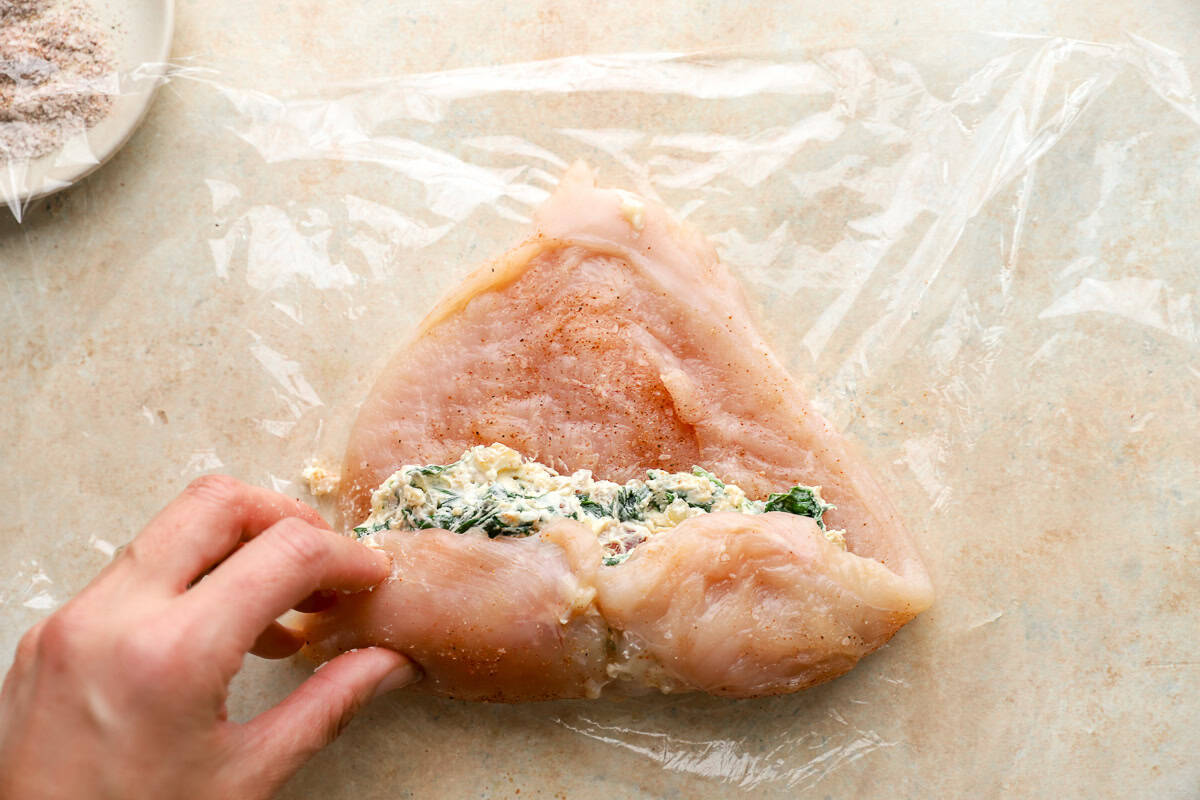 rolling a raw seasoned chicken breast to contain filling.