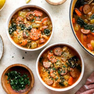 overhead view of bowls of chicken sausage soup topped with parsley and parmesan cheese.