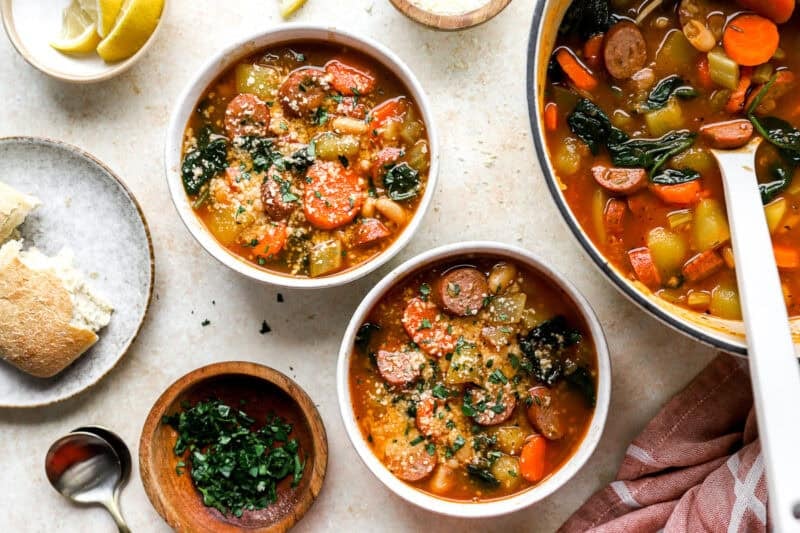 overhead view of bowls of chicken sausage soup topped with parsley and parmesan cheese.