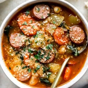 overhead view of a bowl of chicken sausage soup topped with parmesan and parsley with a spoon.