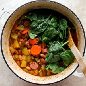 wilting spinach into chicken sausage soup in a pot.