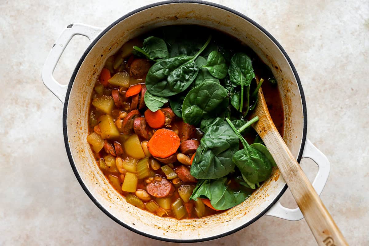wilting spinach into chicken sausage soup in a pot.