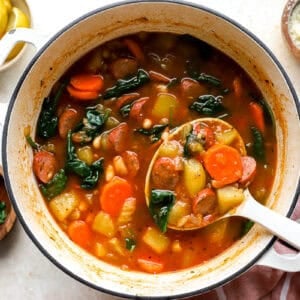scooping a ladleful of chicken sausage soup from a pot.