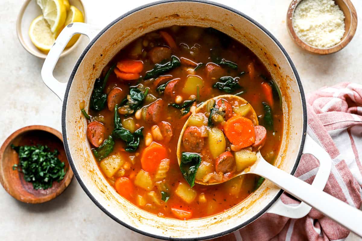 scooping a ladleful of chicken sausage soup from a pot.