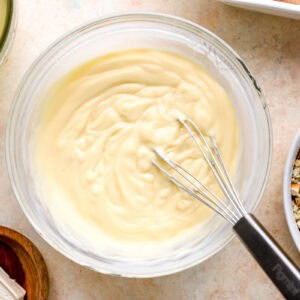 cream of chicken soup mixed with sour cream and chicken broth in a glass bowl with a whisk.
