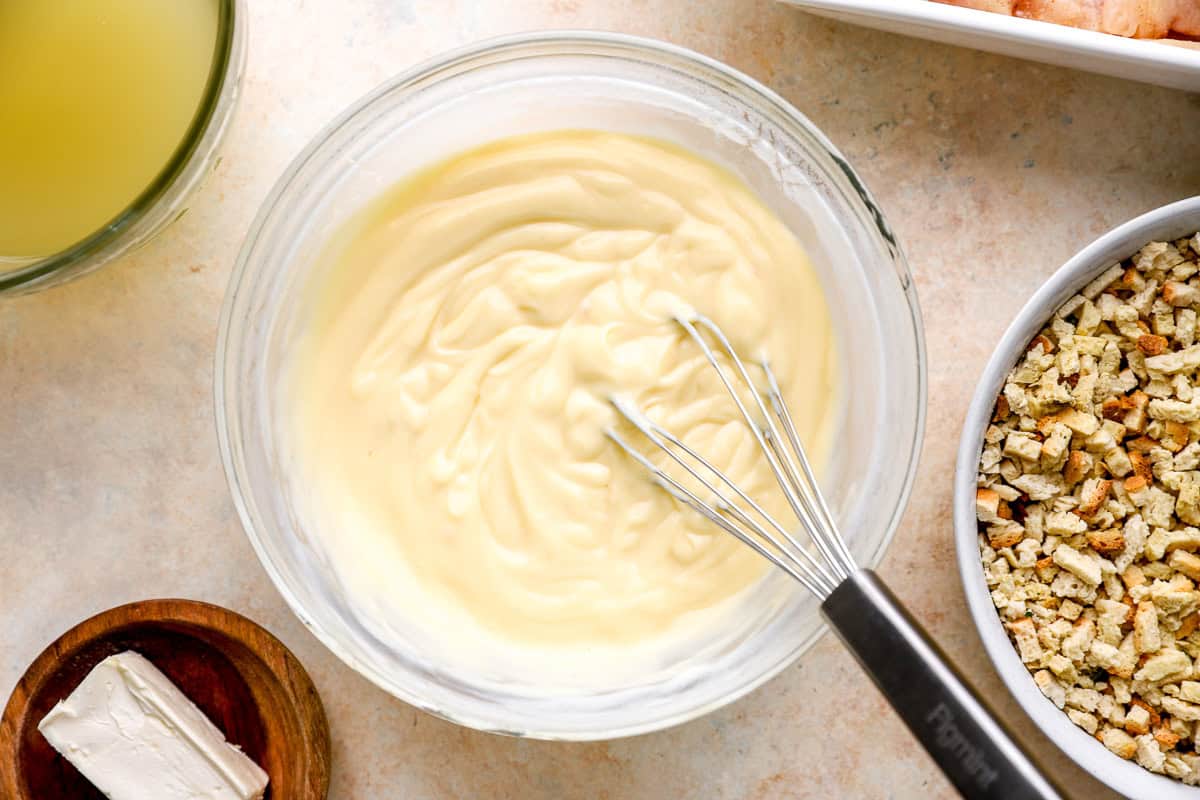 cream of chicken soup mixed with sour cream and chicken broth in a glass bowl with a whisk.