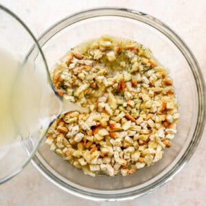 pouring chicken broth over dry stuffing mix in a glass bowl.