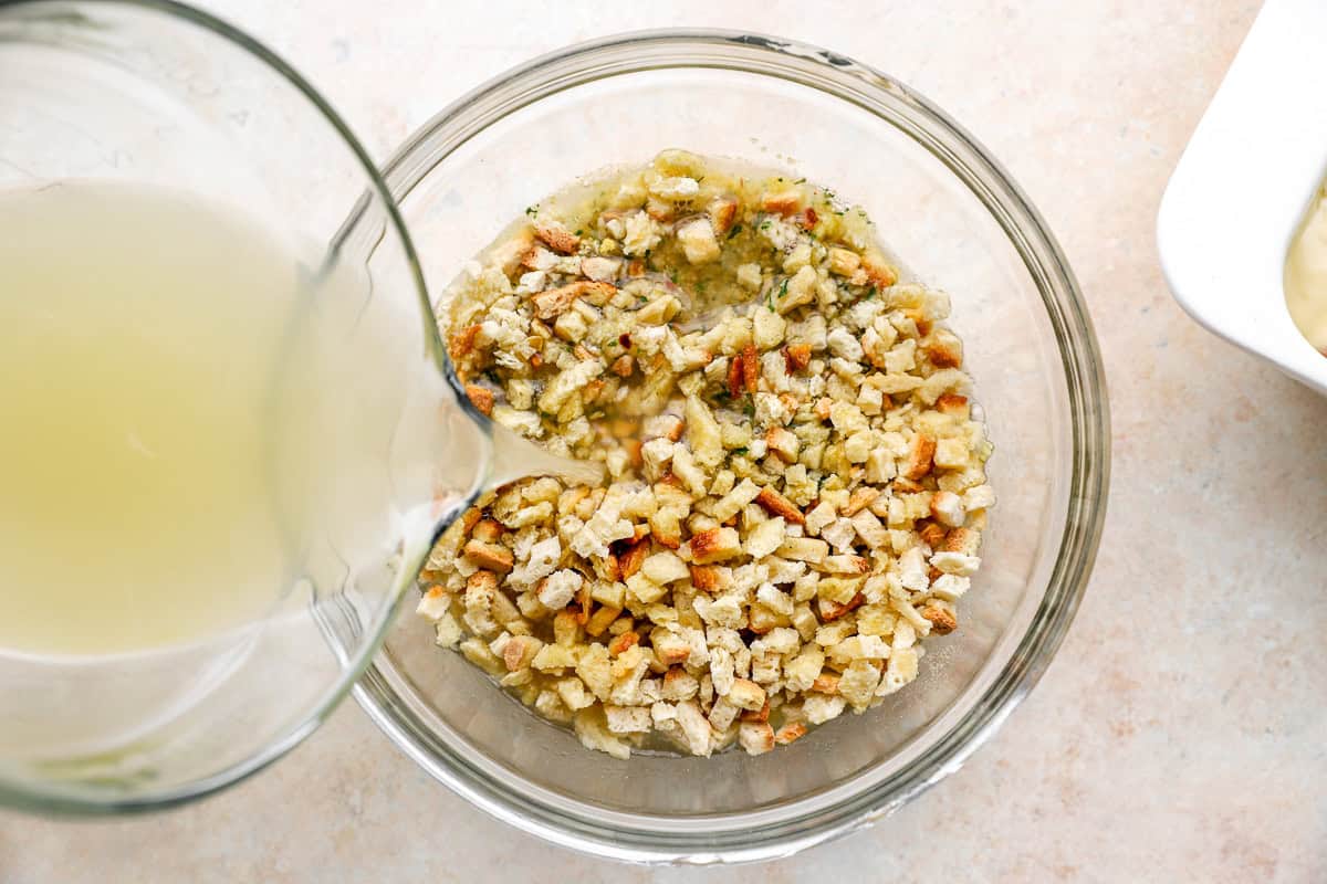 pouring chicken broth over dry stuffing mix in a glass bowl.