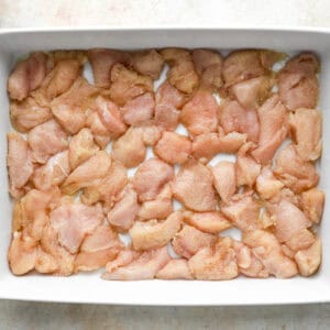 seasoned sliced raw chicken pieces in the bottom of a casserole dish.