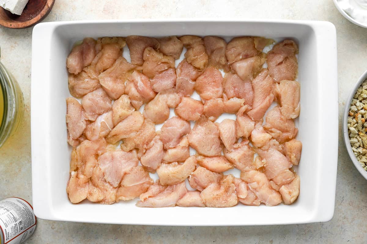 seasoned sliced raw chicken pieces in the bottom of a casserole dish.