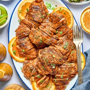 overhead view of sliced chipotle orange chicken on an oval platter with orange wheels and cilantro.