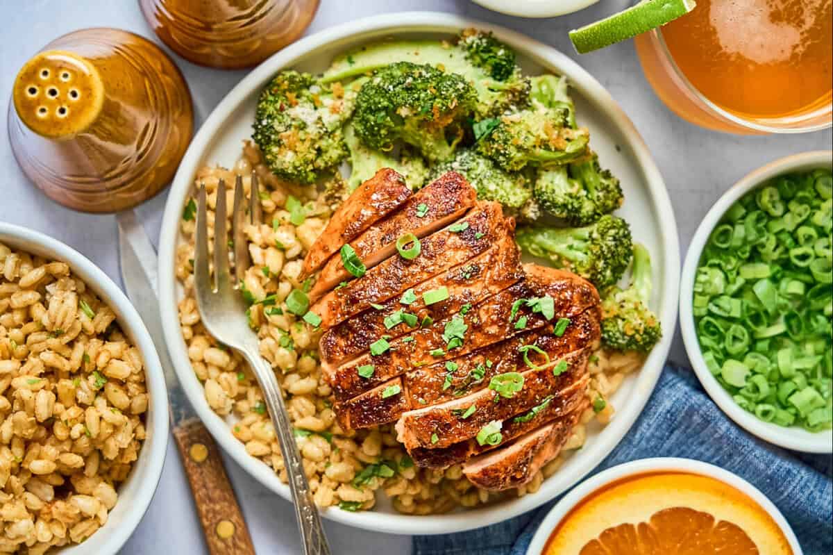 a sliced chipotle orange chicken thigh over couscous with broccoli and a fork.