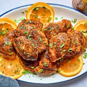overhead view of chipotle orange chicken on an oval platter with orange wheels and cilantro.