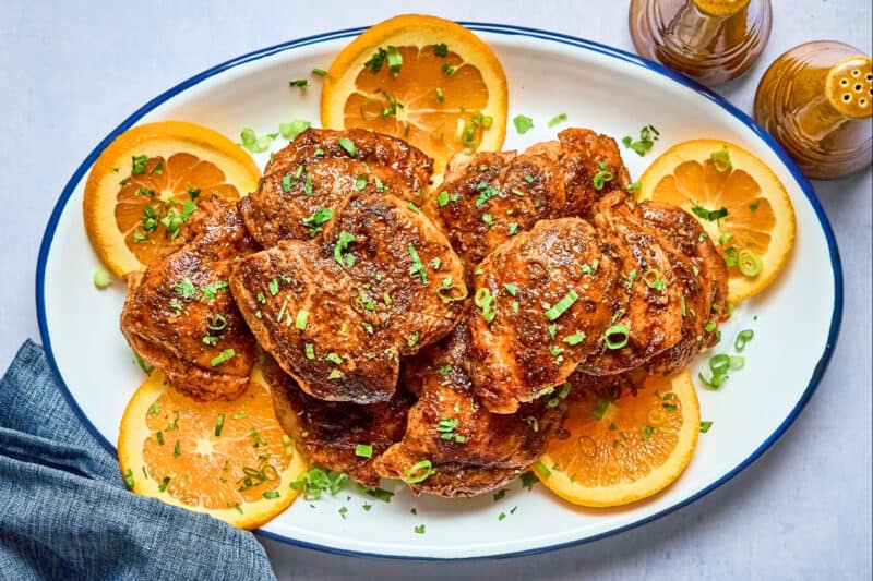 overhead view of chipotle orange chicken on an oval platter with orange wheels and cilantro.