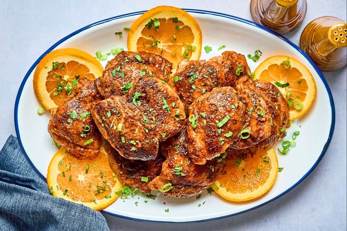 Chipotle orange chicken thighs on an oval platter with orange wheels and cilantro.
