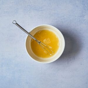 orange juice in a white bowl with a mini whisk.