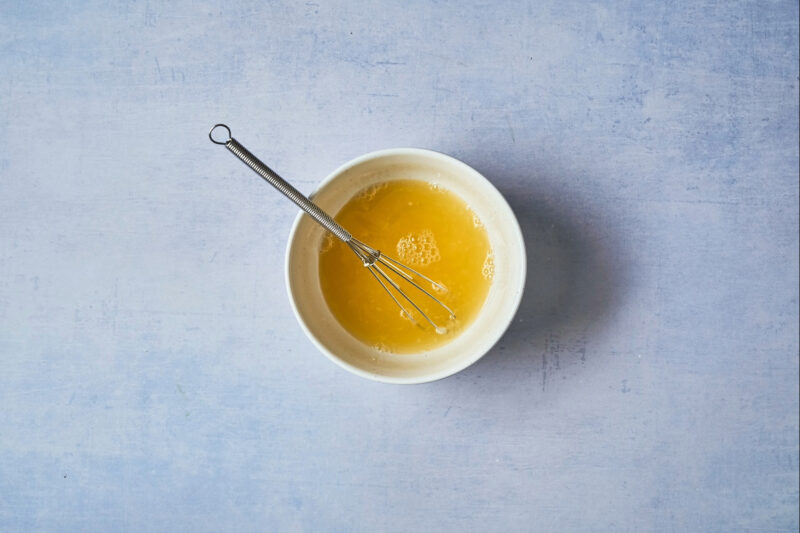 orange juice in a white bowl with a mini whisk.
