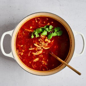 adding cilantro to pozole rojo in a dutch oven.