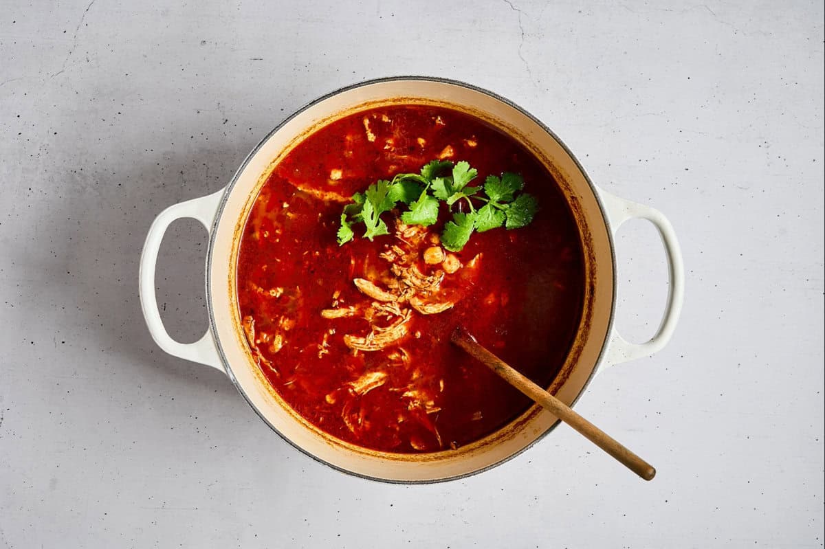 adding cilantro to pozole rojo in a dutch oven.