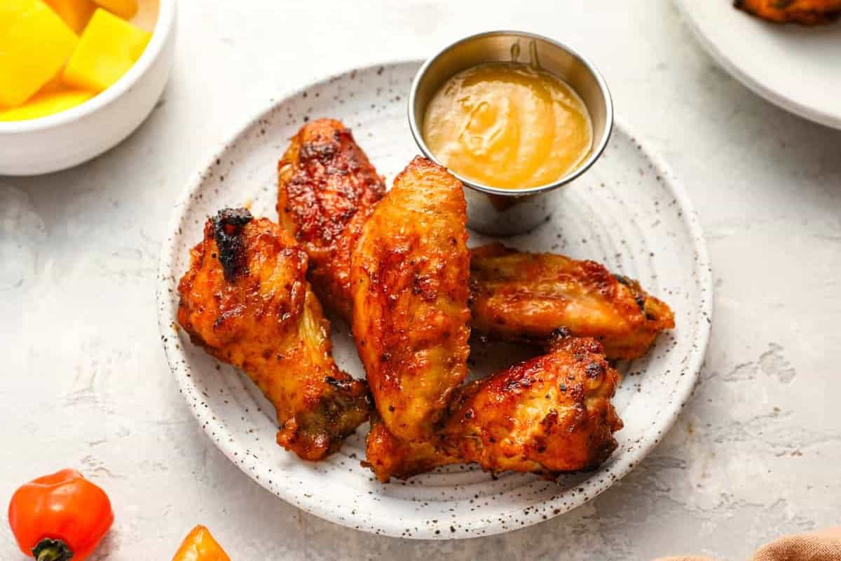 a serving of baked mango habanero chicken wings on a speckled plate with a side of mango habanero sauce.