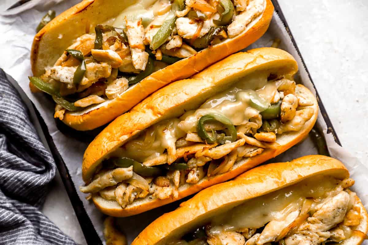 partial overhead view of three chicken philly cheesesteak hoagies on a baking sheet.