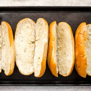 four buttered hoagie rolls on a grill pan.