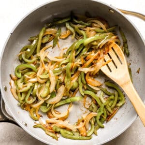 sautéeing sliced peppers and onions in a pan with a wooden spoon.