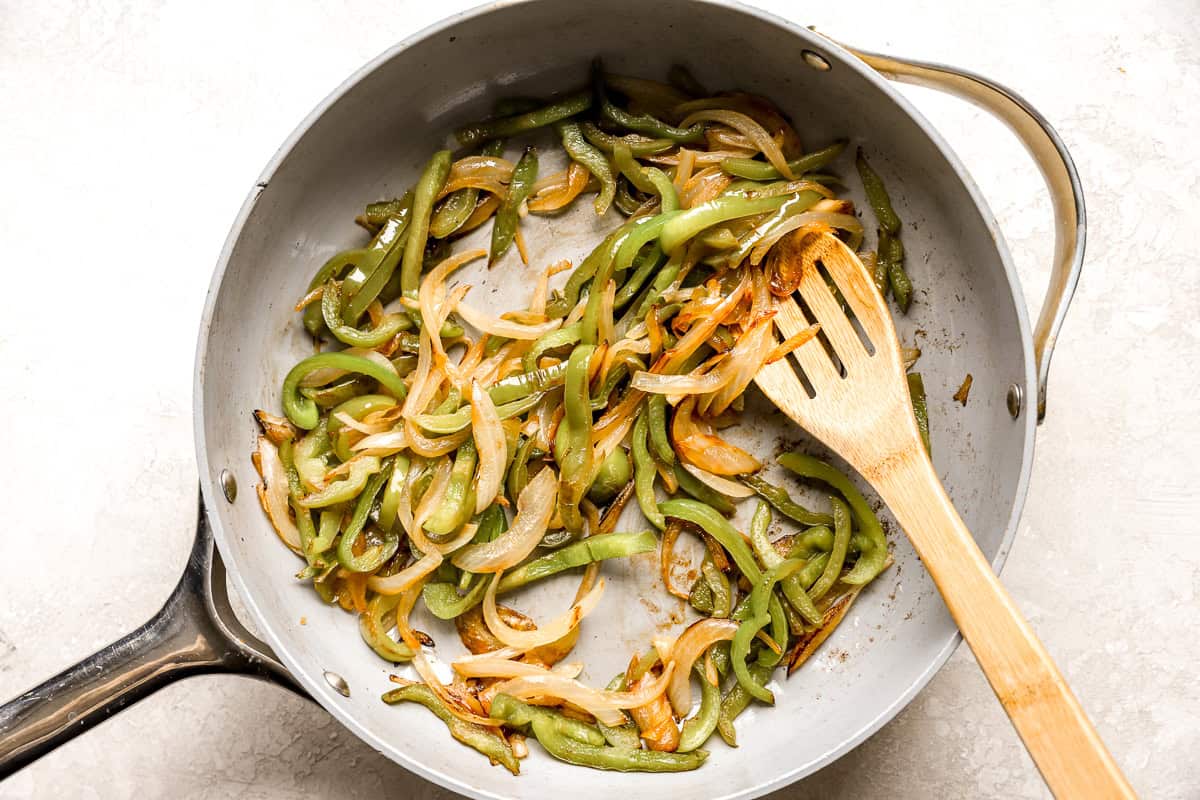 sautéeing sliced peppers and onions in a pan with a wooden spoon.