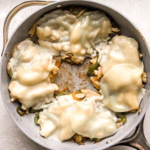 melted cheese slices over chicken and veggies in a pan.