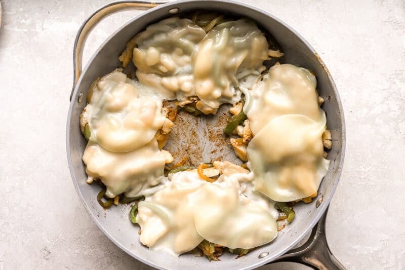 melted cheese slices over chicken and veggies in a pan.