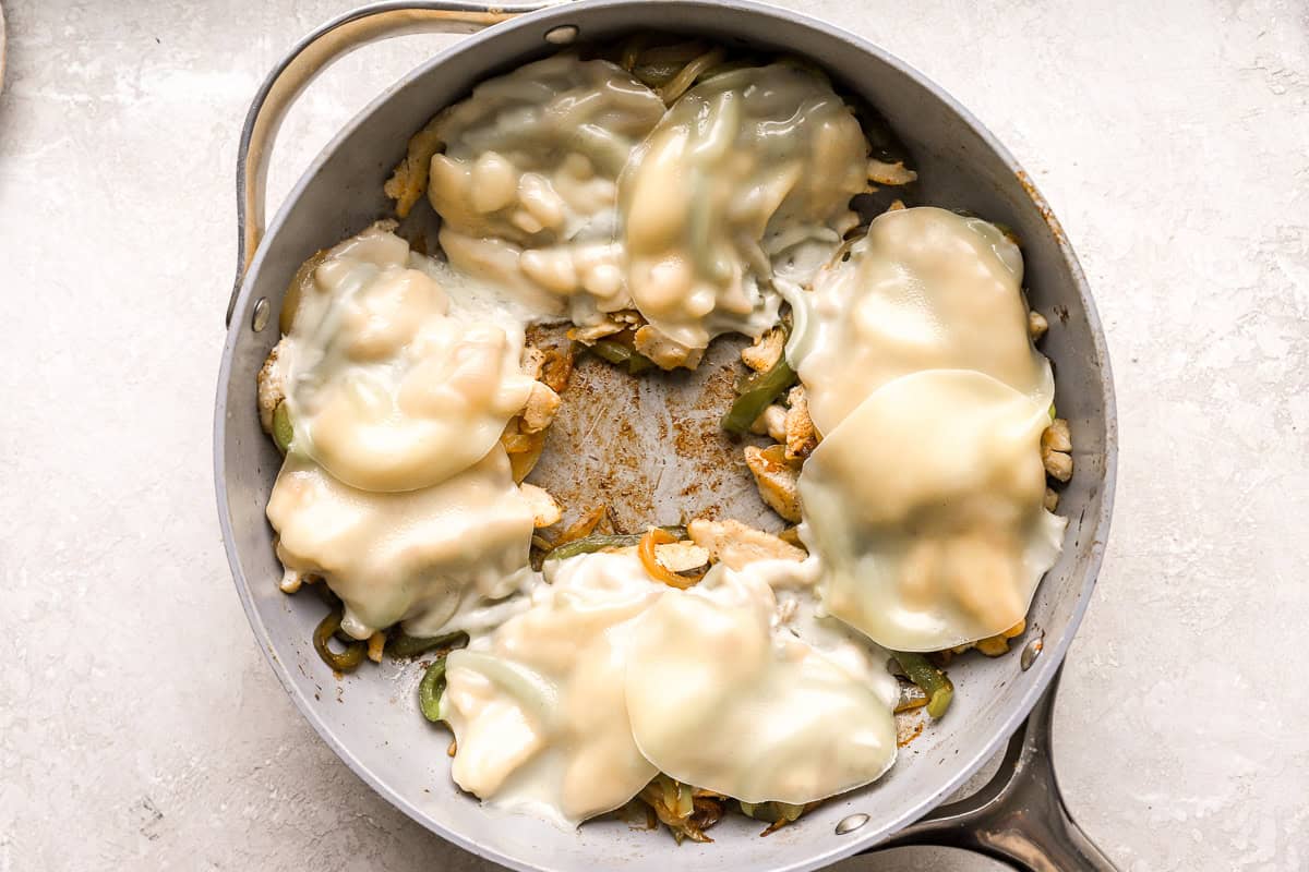 melted cheese slices over chicken and veggies in a pan.