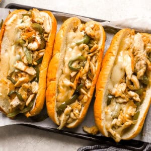 three chicken cheesesteak hoagies on a lined baking sheet.