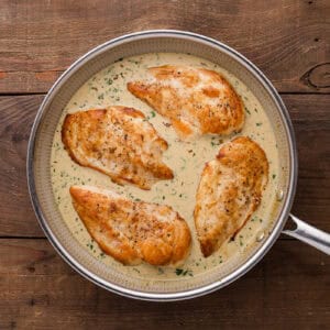 four cooked chicken breasts in creamy cilantro lime sauce in a skillet.