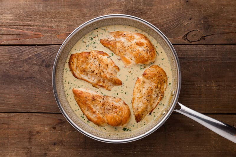 four cooked chicken breasts in creamy cilantro lime sauce in a skillet.