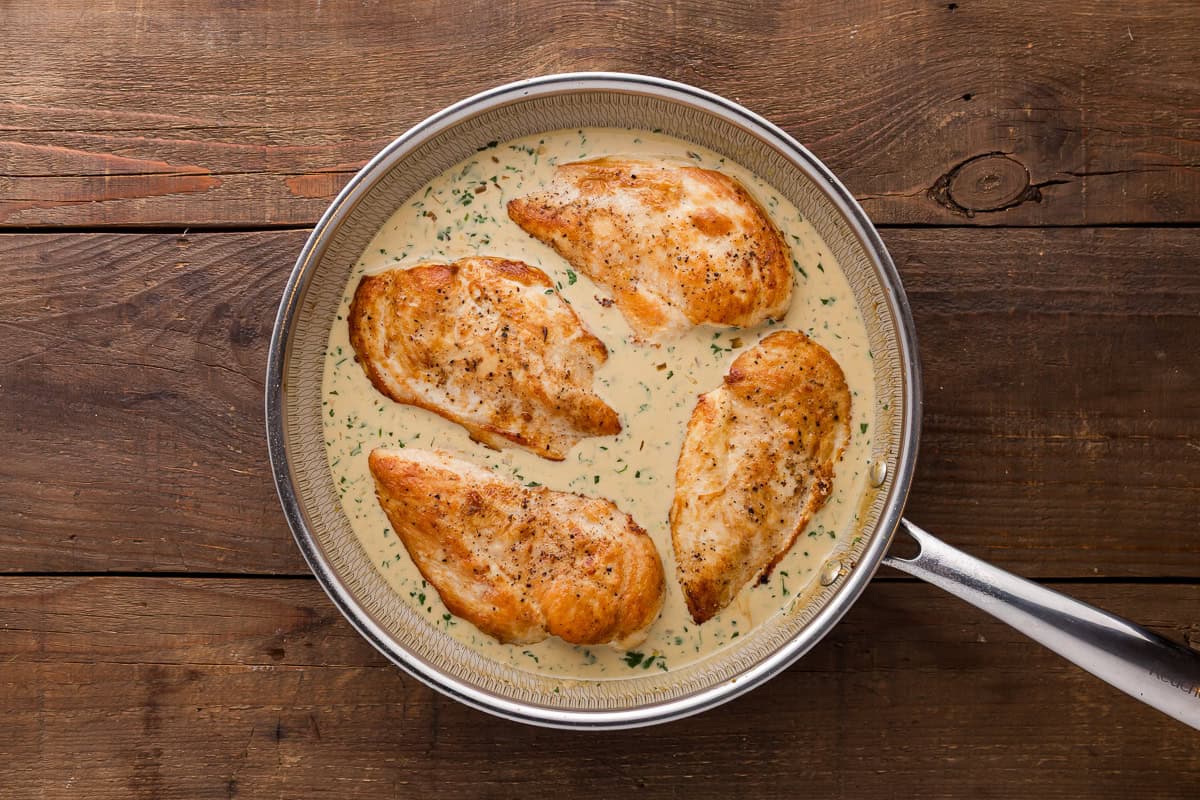 four cooked chicken breasts in creamy cilantro lime sauce in a skillet.