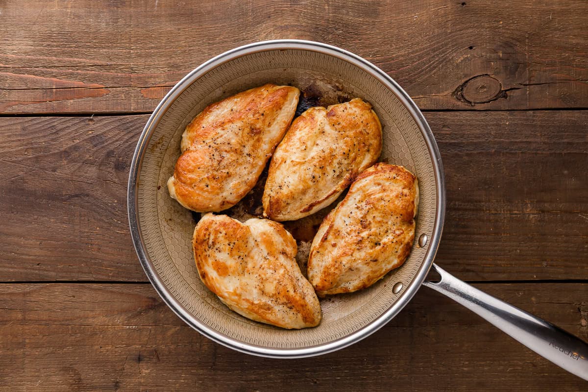 four seared chicken breasts in a skillet.