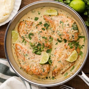 overhead view of creamy cilantro lime chicken in a skillet with lime wedges.