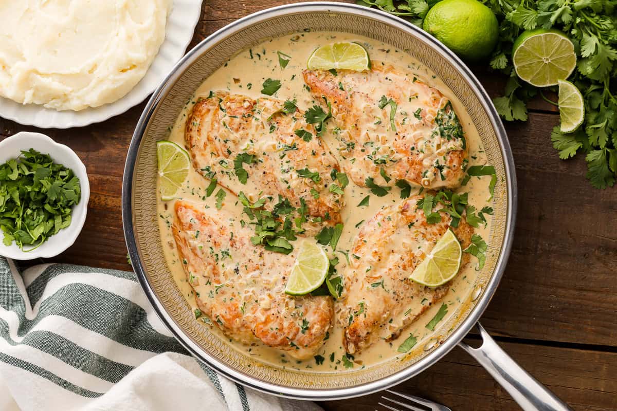 overhead view of creamy cilantro lime chicken in a skillet with lime wedges.