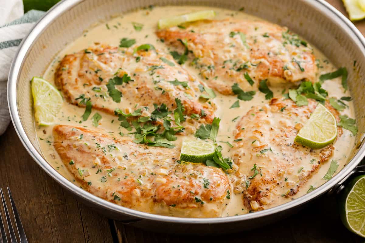 closeup three-quarters view of creamy cilantro lime chicken breasts in a skillet with lime slices.