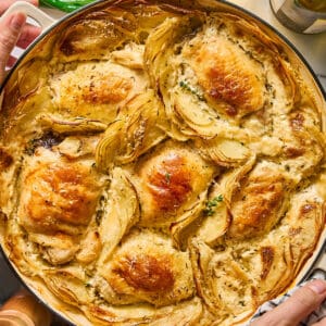 holding a braiser with chicken thighs and potatoes dauphinoise.