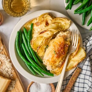 a serving of chicken thighs and potatoes dauphinoise on a white plate with green beans and a fork.