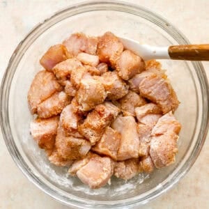 raw chicken bites coated in seasonings in a glass bowl with a rubber spatula.
