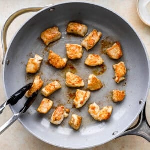 searing chicken bites in a pan with tongs.