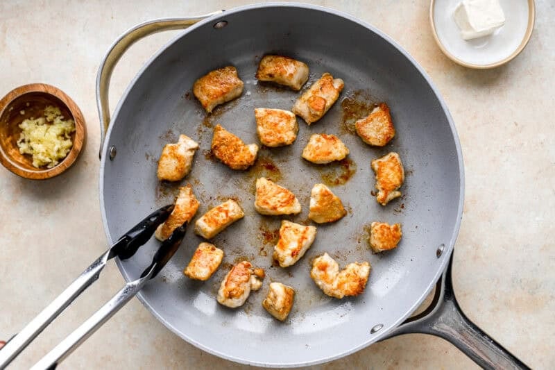 searing chicken bites in a pan with tongs.
