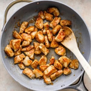 tossing chicken bites in garlic butter sauce with a wooden spoon.