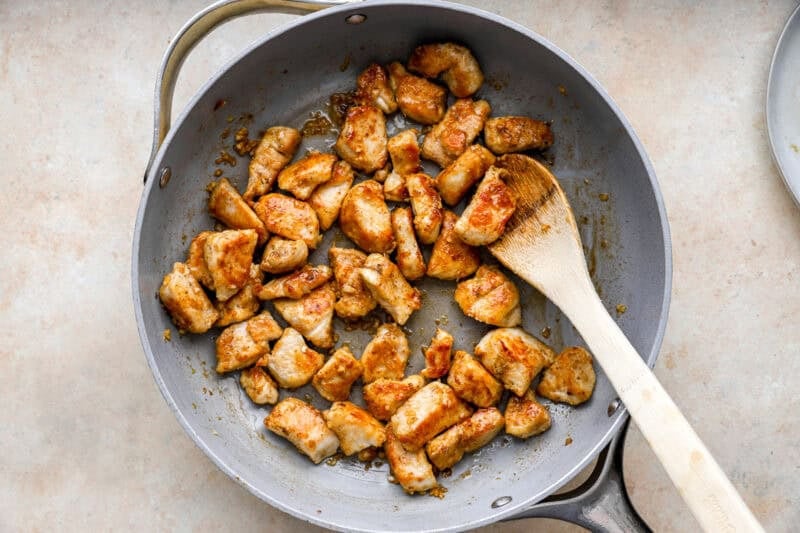 tossing chicken bites in garlic butter sauce with a wooden spoon.